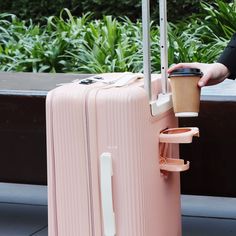 a person holding a pink piece of luggage next to a coffee cup on the ground