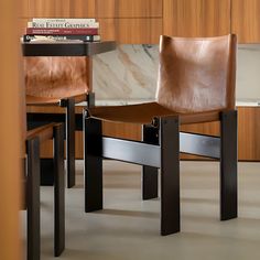 two leather chairs sitting next to each other in front of a wooden table and bookshelf