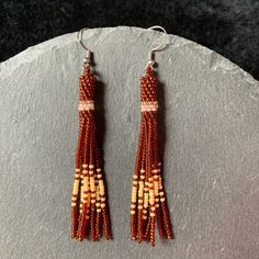 two pairs of beaded earrings sitting on top of a gray stone slab next to a rock