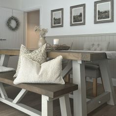 a wooden bench sitting in front of a kitchen table with pillows on top of it