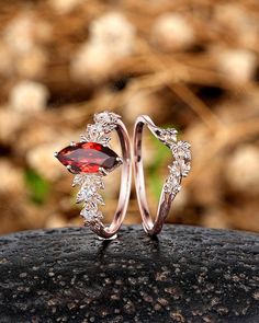 two wedding rings with garnetia and diamonds on top of a rock in the grass