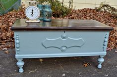 a blue chest with two clocks on top and some leaves in the ground behind it