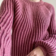 a woman in a pink sweater holding her hand up to her chest and looking at the camera