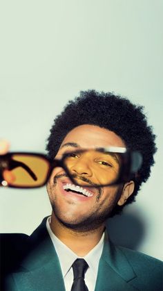 a man in a suit and tie is holding up his glasses to look at the camera