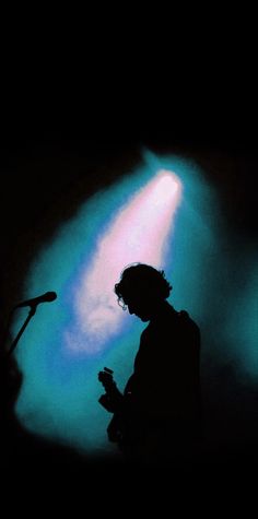 the silhouette of a person standing in front of a microphone with a blue light behind them