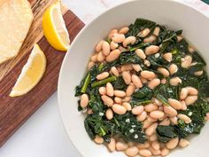 a white bowl filled with beans and spinach next to sliced lemons on a cutting board