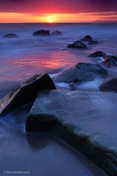 the sun is setting over some rocks in the water at the beach with waves crashing on them