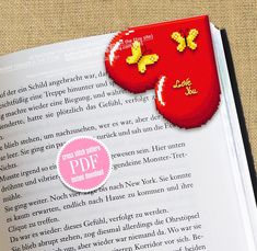 an open book with two cross stitched hearts on the pages and a pink ribbon pinned to it