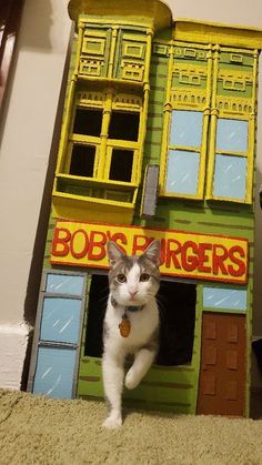 a cat is standing in the doorway of a doll's house made out of cardboard