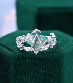 an engagement ring with green stones and leaves on the band, sitting on top of a velvet box