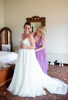 two women standing next to each other in front of a bed and mirror with their arms around each other