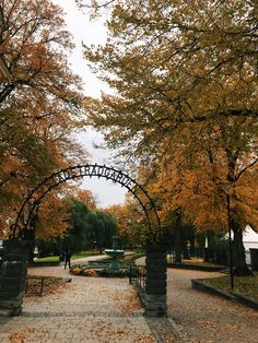 an archway in the middle of a park with yellow leaves on the ground and people walking under it