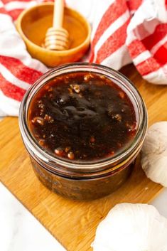 a jar of barbecue sauce sitting on top of a wooden cutting board next to garlic