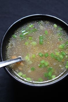 a bowl filled with soup on top of a black table next to a silver spoon