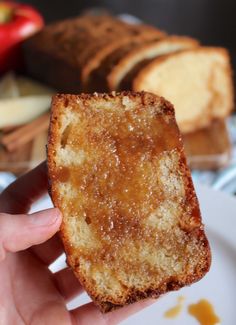 a person holding up a piece of bread on a plate with apples in the background