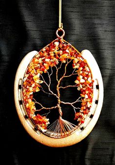 a tree of life ornament hanging from a hook on a black background,