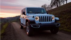 a white jeep driving down a dirt road next to a hill at sunset with trees in the background