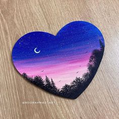 a painted heart on a wooden surface with trees and a moon in the sky at night