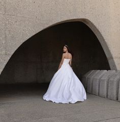 a woman in a white wedding dress is standing under a concrete arch and posing for the camera