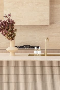 A kitchen features brushed brass tapware and travertine stone feature tiles. Tiled Island Bench Kitchen, Brass Benchtop, Travertine Benchtop, Tiled Kitchen Island, Fluted Travertine, Travertine Kitchen, Travertine Countertops, Brushed Brass Kitchen, Brass Kitchen Island