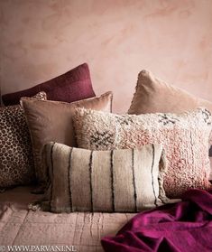 a bed topped with lots of pillows next to a pink wall