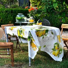 a table covered with a yellow and white floral print sitting in the grass next to two wooden chairs