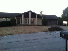 a house that is sitting in the middle of a street with grass and bushes around it