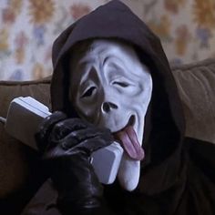 a person wearing a mask and holding a cell phone to their face while sitting on a couch