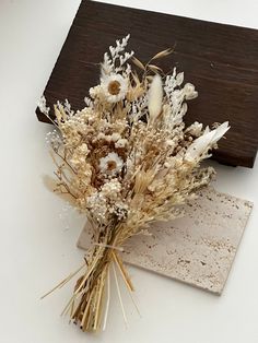 dried flowers sitting on top of a piece of paper next to a wooden block with a sign