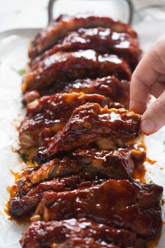 someone is picking up some ribs from the tray on the table, with sauce all over them