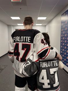 two hockey players are walking down the hall with their backs to each other and hugging