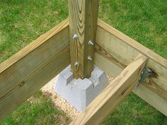 a wooden post with nails sticking out of it in the grass next to a cement block