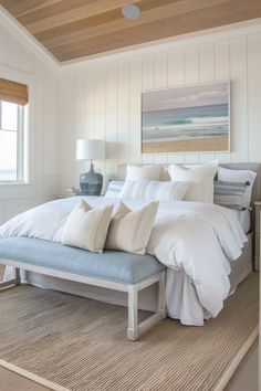 Bright, cozy bedroom with a large bed, soft white and blue pillows, wooden bench, textured rug, and beach painting on a paneled wall. Natural light from a window. Neutral Coastal Bedroom, Tropical Bedrooms, Deco Studio, Beach Room