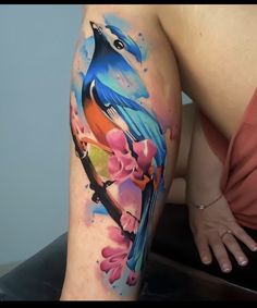 a woman's thigh with a colorful bird on the branch and flowers painted on it