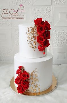 a three tiered white cake with red flowers on the top and gold trimmings