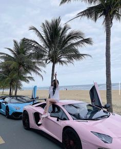 a woman sitting on the hood of a pink sports car next to two other cars