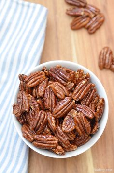 a white bowl filled with pecans sitting on top of a wooden table next to a blue and white towel