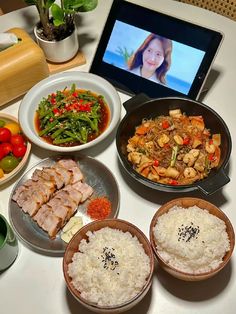 a table topped with plates of food and bowls of rice next to a laptop computer