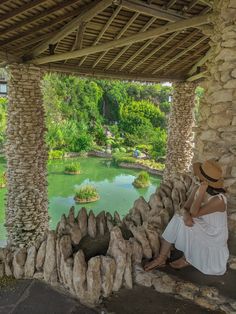 a woman sitting on the side of a stone wall next to a lake