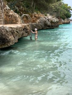 a woman standing in the water near some rocks