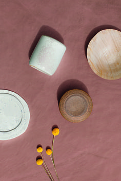 three bowls and two plates on a pink surface with yellow flowers in the foreground