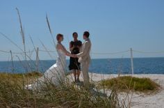 three people standing on top of a beach next to the ocean with grass in front of them