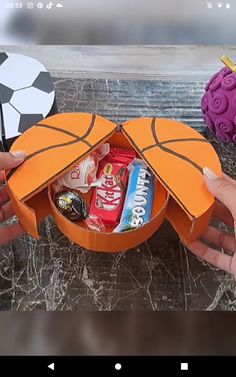 two hands holding an orange basketball shaped box filled with candy and candies next to a soccer ball