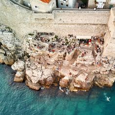 an aerial view of people sitting on the rocks by the water