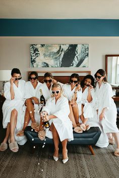 a group of women in white robes sitting on a couch with champagne bottles and glasses