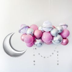 balloons and stars are floating in the air next to a crescent shaped balloon on a white wall