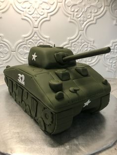 a green tank cake sitting on top of a silver plate covered in frosted icing