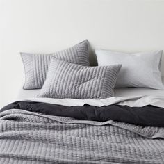 an unmade bed with grey and white pillows