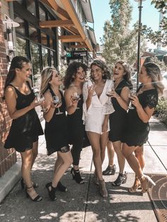 group of young women standing on sidewalk with wine glasses in hand and smiling at camera