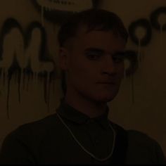 a young man standing in front of a wall with graffiti on it's walls